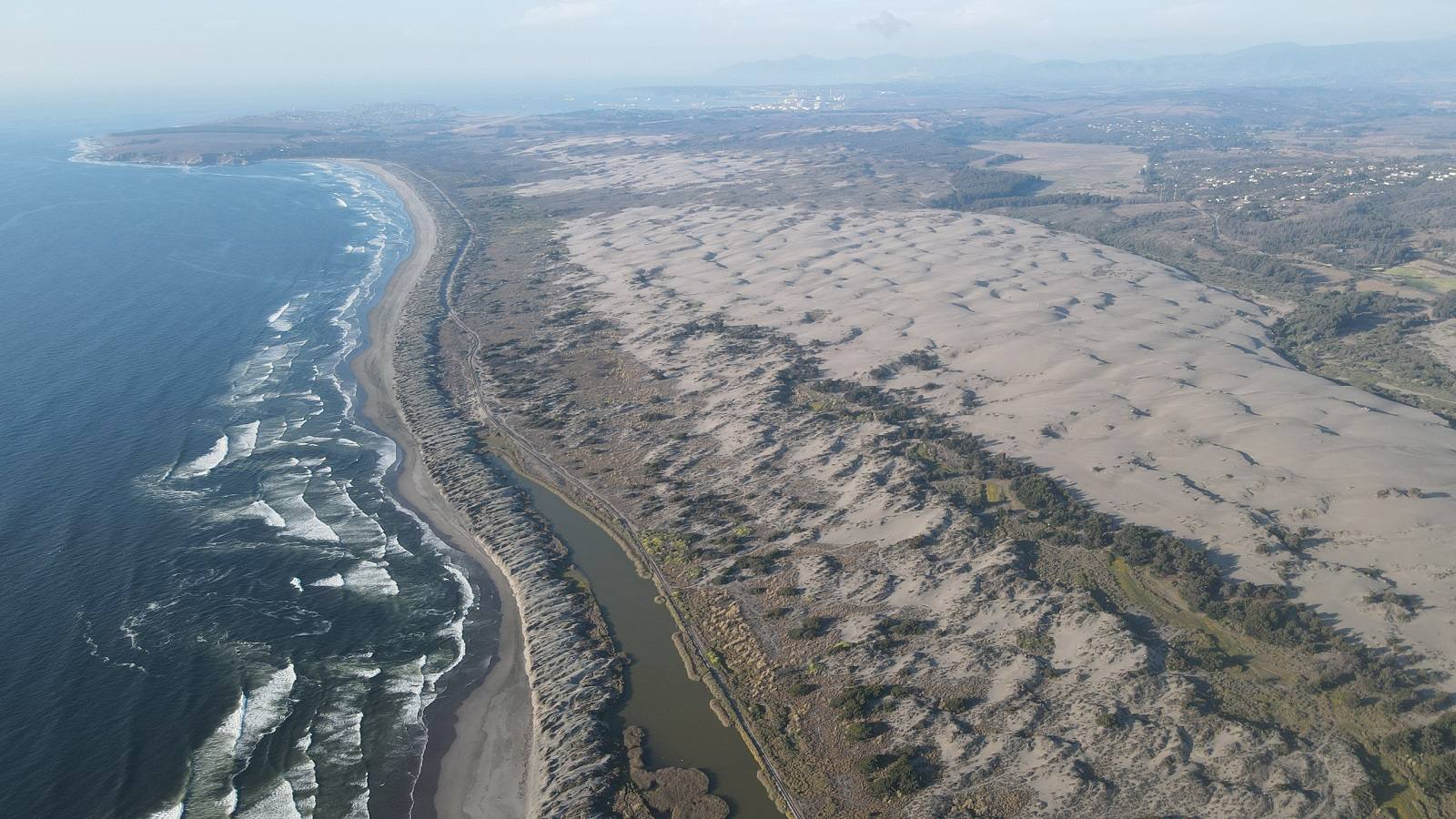 Costa con dunas y un estero paralelo a la playa, con Quintero al fondo
